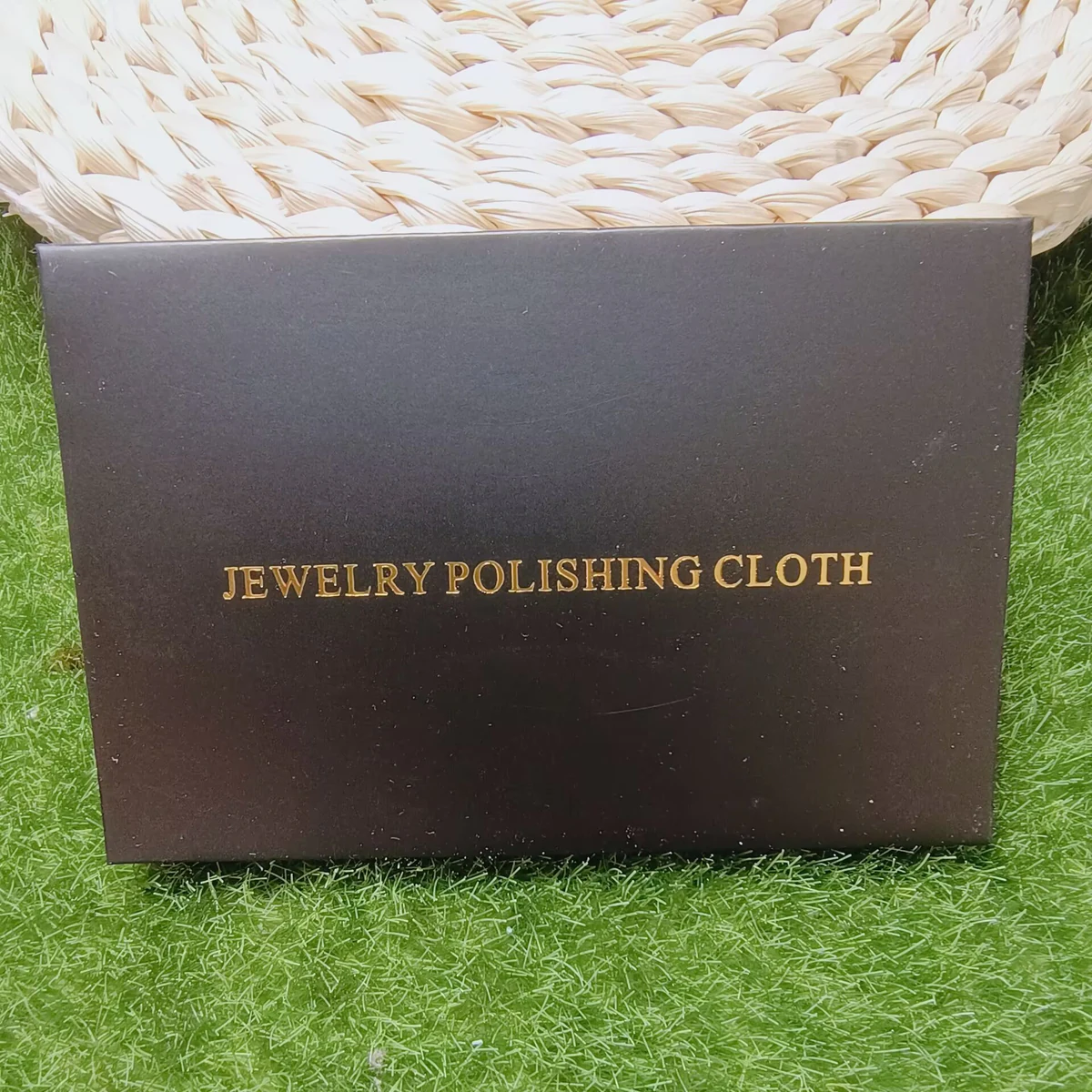 Single black jewelry polishing cloth envelope with gold foil lettering on a green display surface