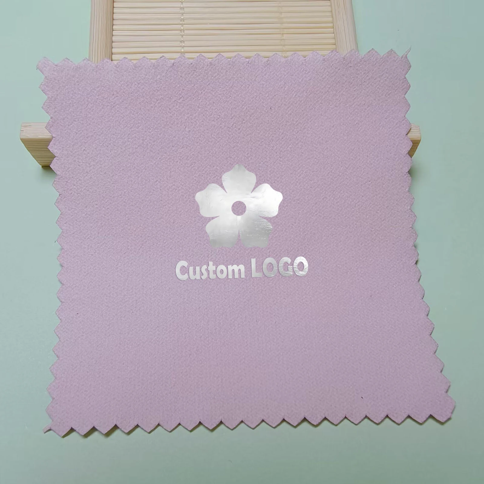 Lavender jewelry polishing cloth with a metallic silver flower logo and zigzag edges