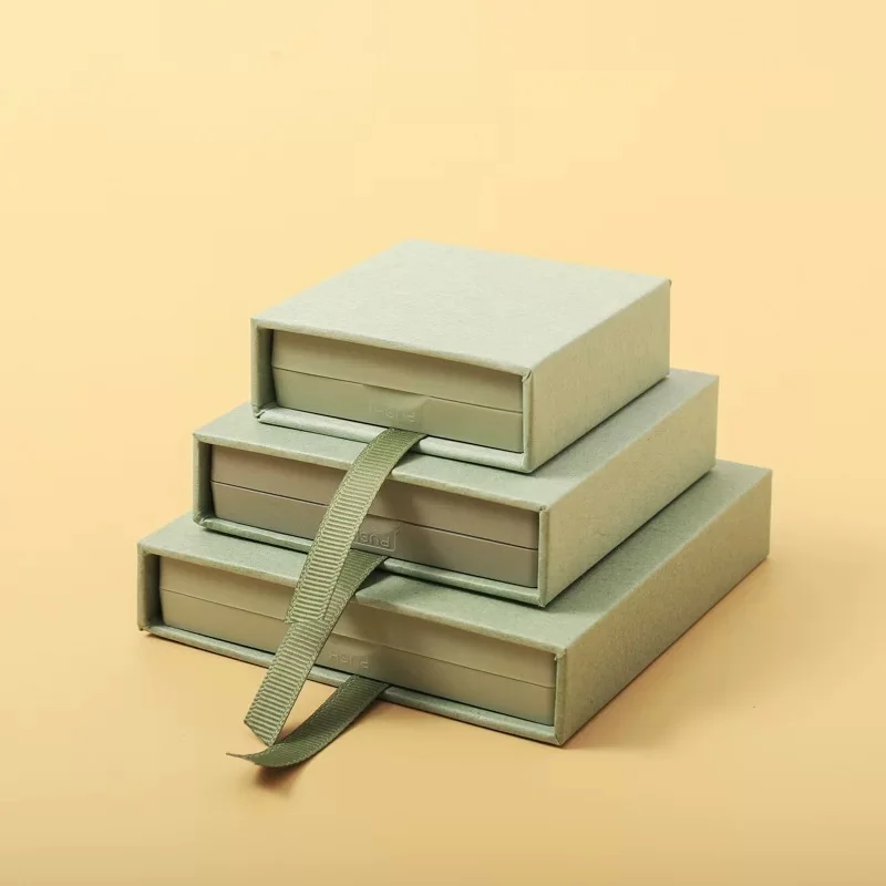 Three sage green sliding drawer jewelry boxes in different sizes with a ribbon pull