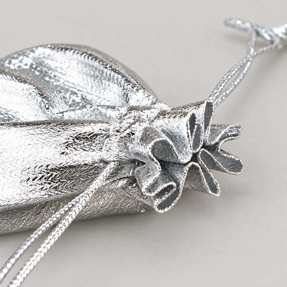 Close-up of the stitched gathered closure and braided cords on a silver metallic jewelry pouch