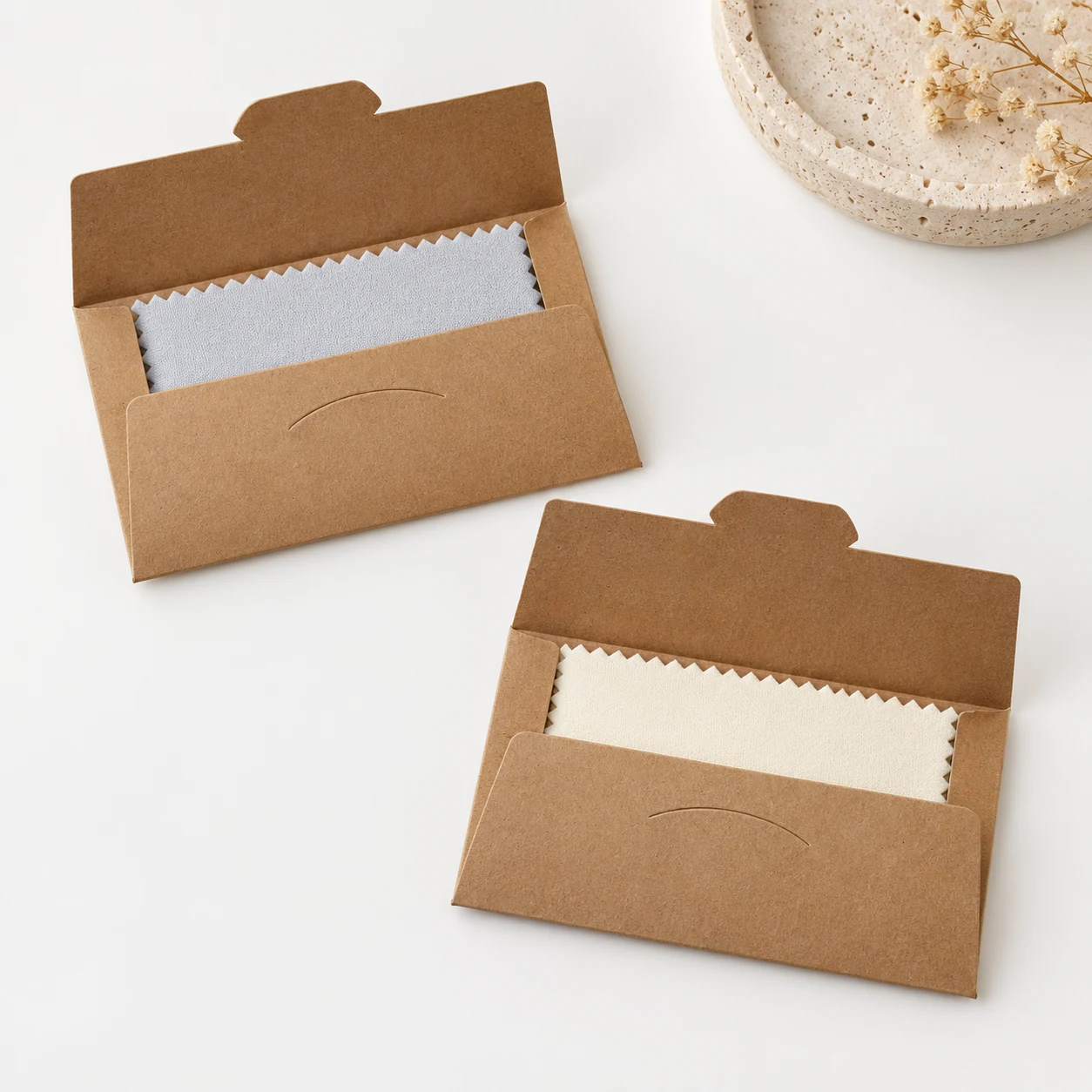 Open kraft paper envelopes holding assorted light gray and cream 6.5 x 10 cm silver polishing cloths