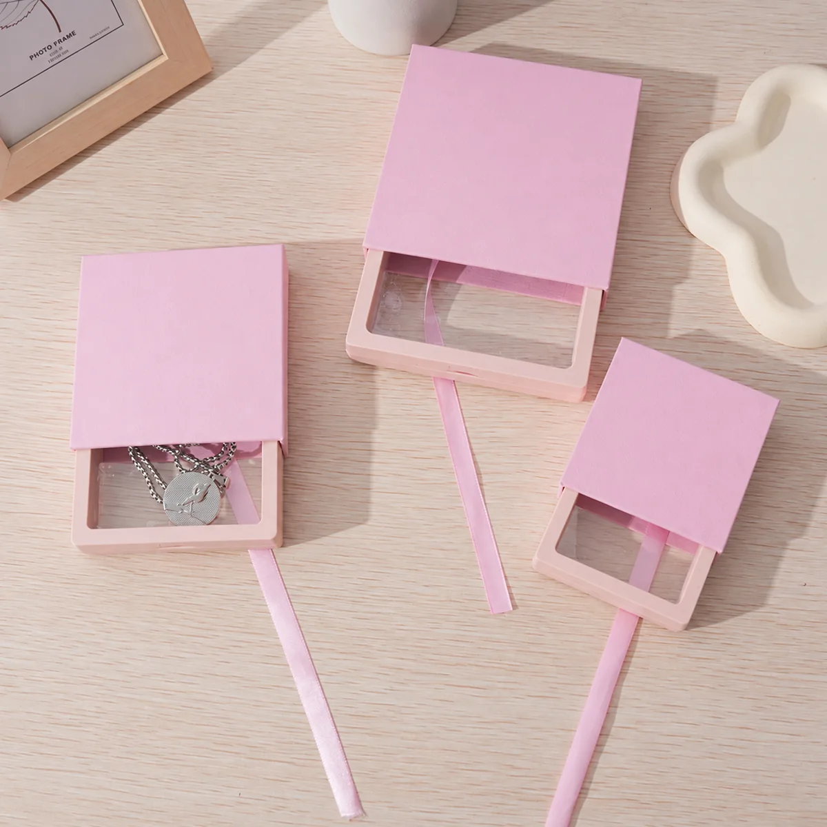 Three pink drawer jewelry boxes with clear suspension film inserts, including one holding a necklace