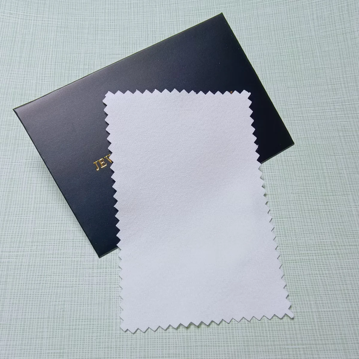 White zigzag-edge jewelry polishing cloth displayed with a black paper envelope